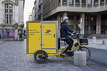 Biosphoto | 2575674 | Letter carrier driving an electric cargo bike on Place Louis Pradel. Parcel delivery and cargo bike body with La Poste logo and the phrase 